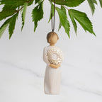 Front view: Dated Ornament of figure holding pierced gold-leaf wreath of hearts. 2024 written on wreath; loop and hook in head