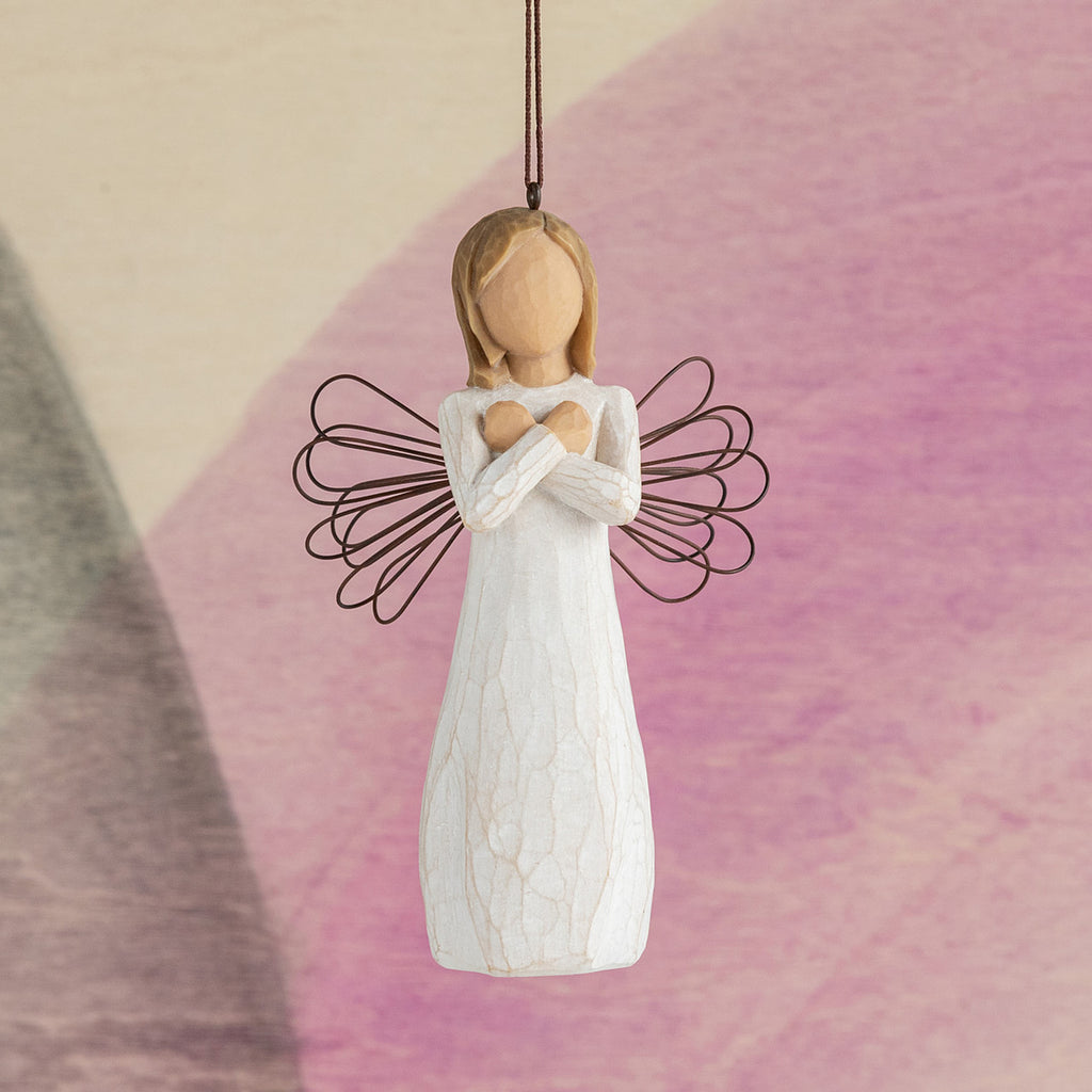 Willow Tree Sign for Love Ornament, 4.5”h hand-painted resin figure in cream dress with wire wings,  with crossed arms meaning "Love" in American Sign Language, brown elastic cord, hanging in front of pink painting