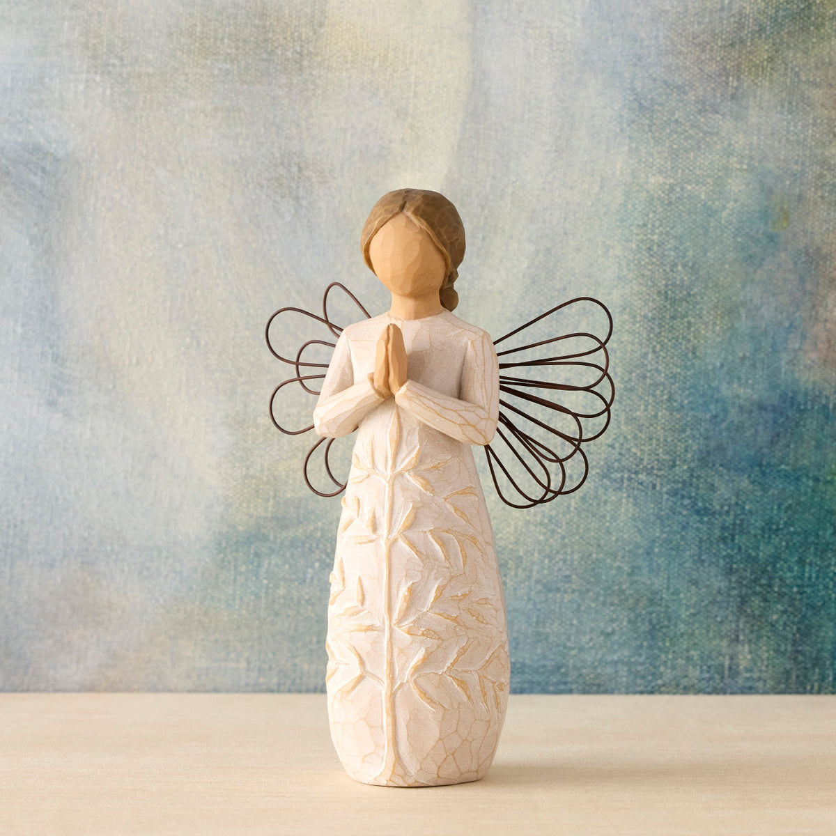 Willow Tree a tree, a prayer, 5.5”h hand-painted standing resin angel figure in cream dress with wire wings, hands in prayer position; tree carving on dress, in front of blue-grey painting