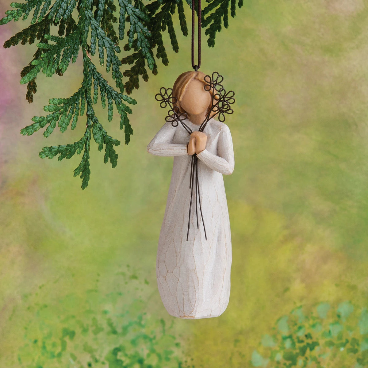 Willow Tree Friendship Ornament, 5.5"h hand-painted resin figure in cream dress holding wire flowers with long stems, brown elastic cord, hanging in front of mossy green painting