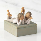 Front/long side view of closed rectangular blue-gray resin box, box; sculpture of two reclining girls on box lid