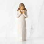 Front view, standing female figure in cream dress, hands surrounding small gold-leaf flame on chest