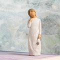 Willow Tree Remember, 5.5”h hand-painted standing resin figure in cream dress holding drooping wire flower in hand, in front of grey painting