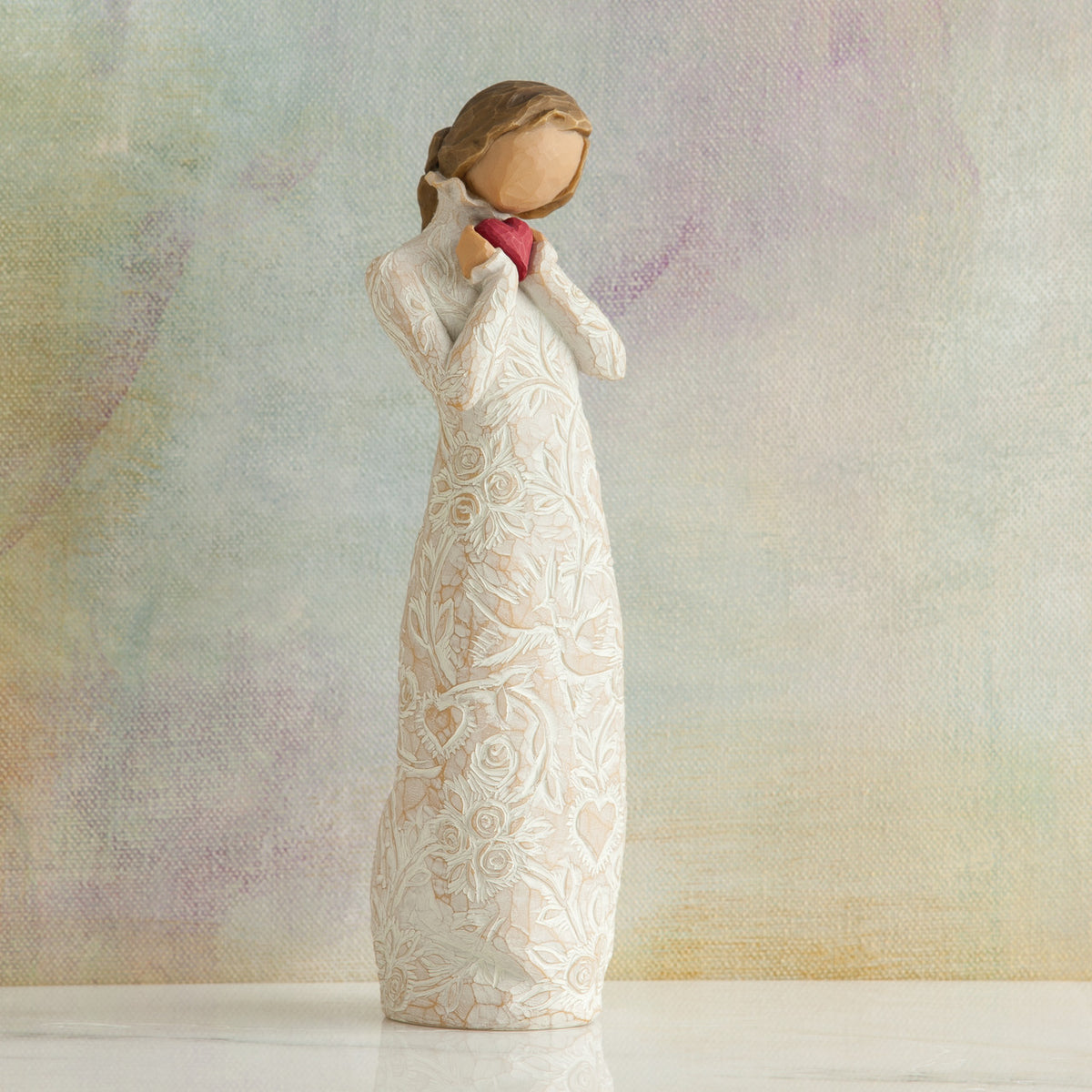 Willow Tree Je t'aime (I Love You), 8.5"h hand-painted standing resin figure holding red heart in cream dress with ruffled neck and carved with hearts, flowers and birds, in front of muted painting