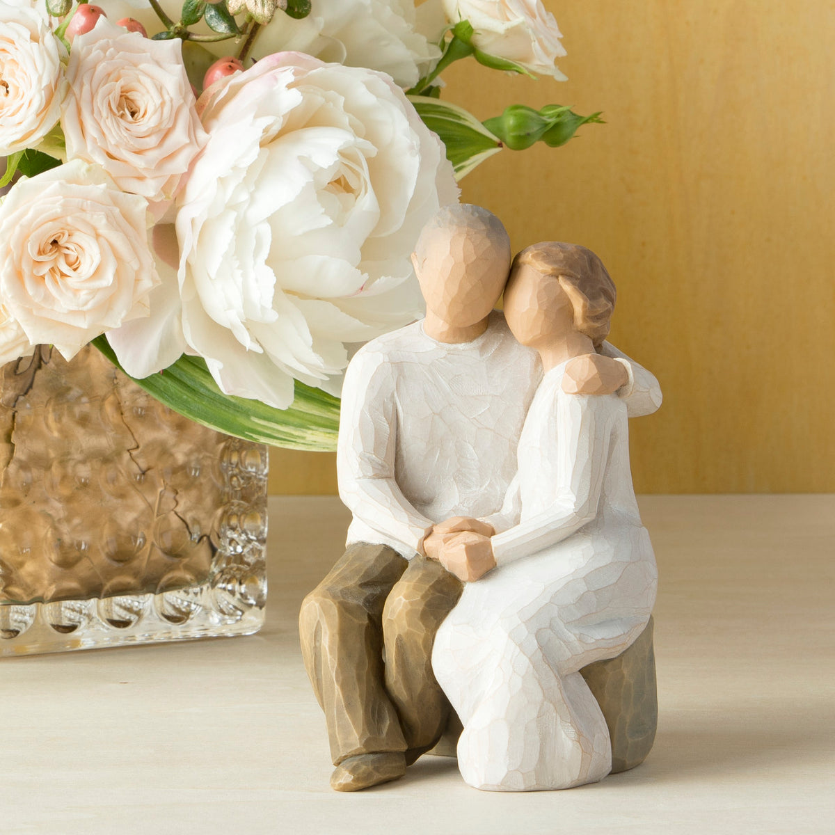 Willow Tree Anniversary, 6”h hand-painted resin figure of older couple sitting on bench holding hands, both in neutral clothing, on table with white roses
