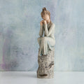 Willow Tree Patience, 7”h hand-painted resin figure in blue/gray dress, hands under chin, sitting on grey rock etched with symbols, in front of muted blue painting