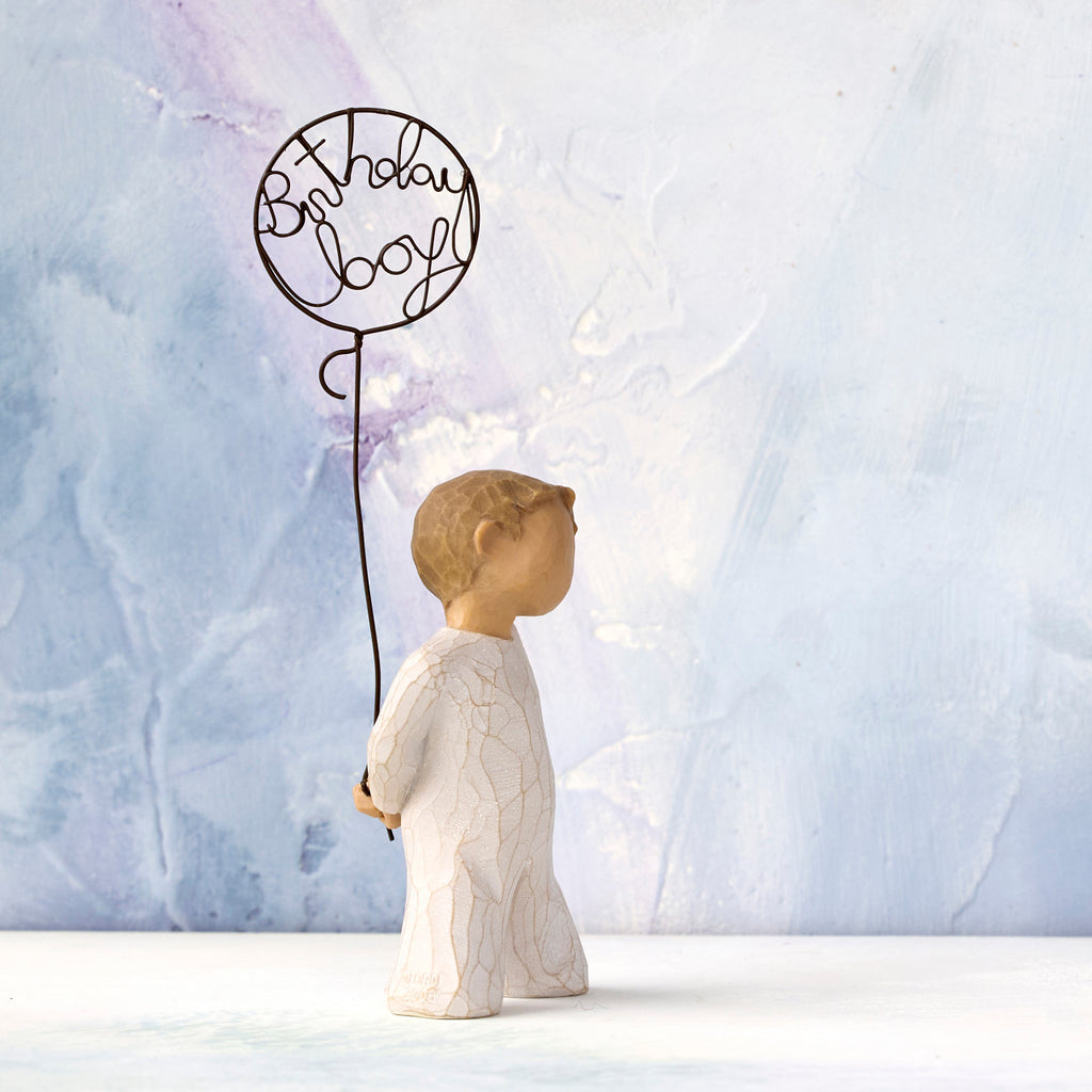 Willow Tree Birthday Boy, 5”h hand-painted standing resin figure in cream onesie, holding wire ballon with 'birthday boy' written in wire, in front of blue painting