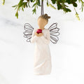 Front view of figure in cream dress with wire wings holding large red apple in hands, ornament hook on head
