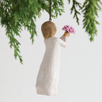 Back view of woman ornament with short brown hair, holding out a bouquet of pink flowers. Brown string attached to top of ornament