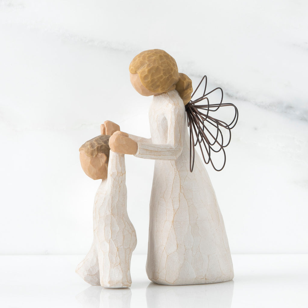 Side view of blonde angel figurine in white dress holding up baby figurine in white