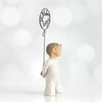 Left side view of little boy with light brown hair holding a wire balloon behind his back. Text on balloon is wire