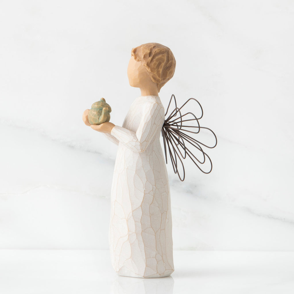 Angel figurine in white with black wings facing the side holding golden teapot figurine