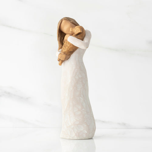 Left view, standing female figure in cream dress, holding golden color puppy in her arms