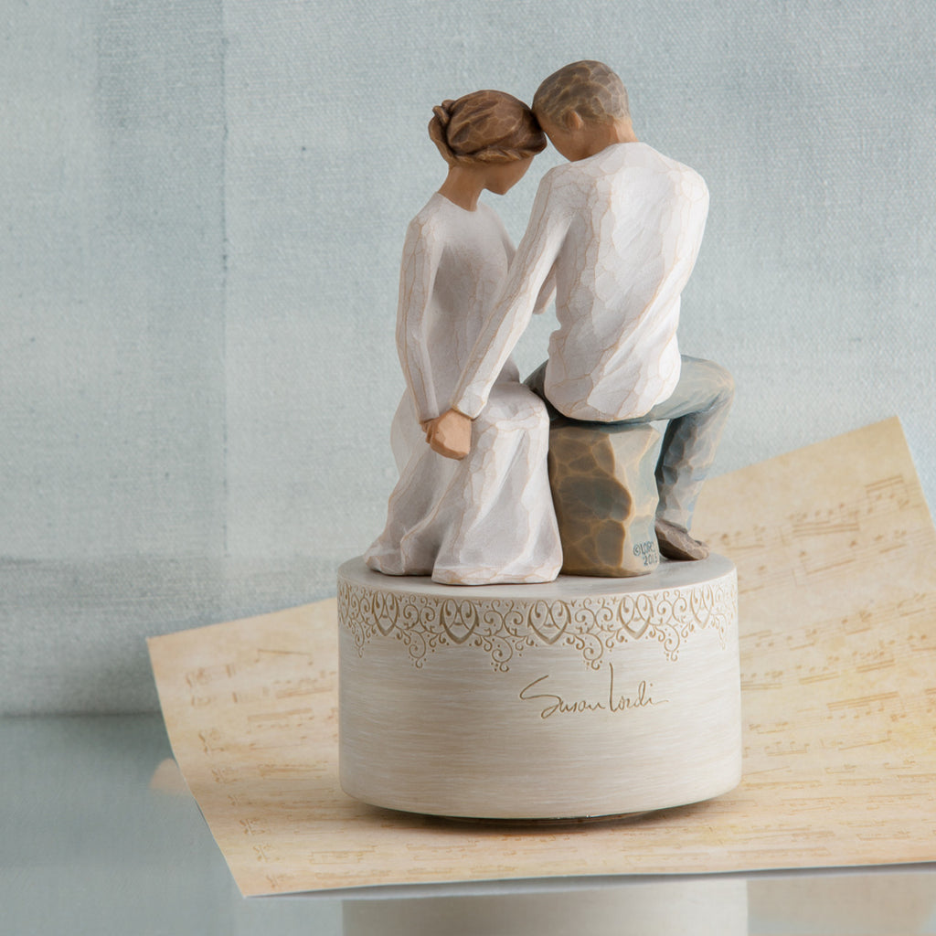Man and woman figurine in white sitting holding hands on round large plaque and tan paper below it