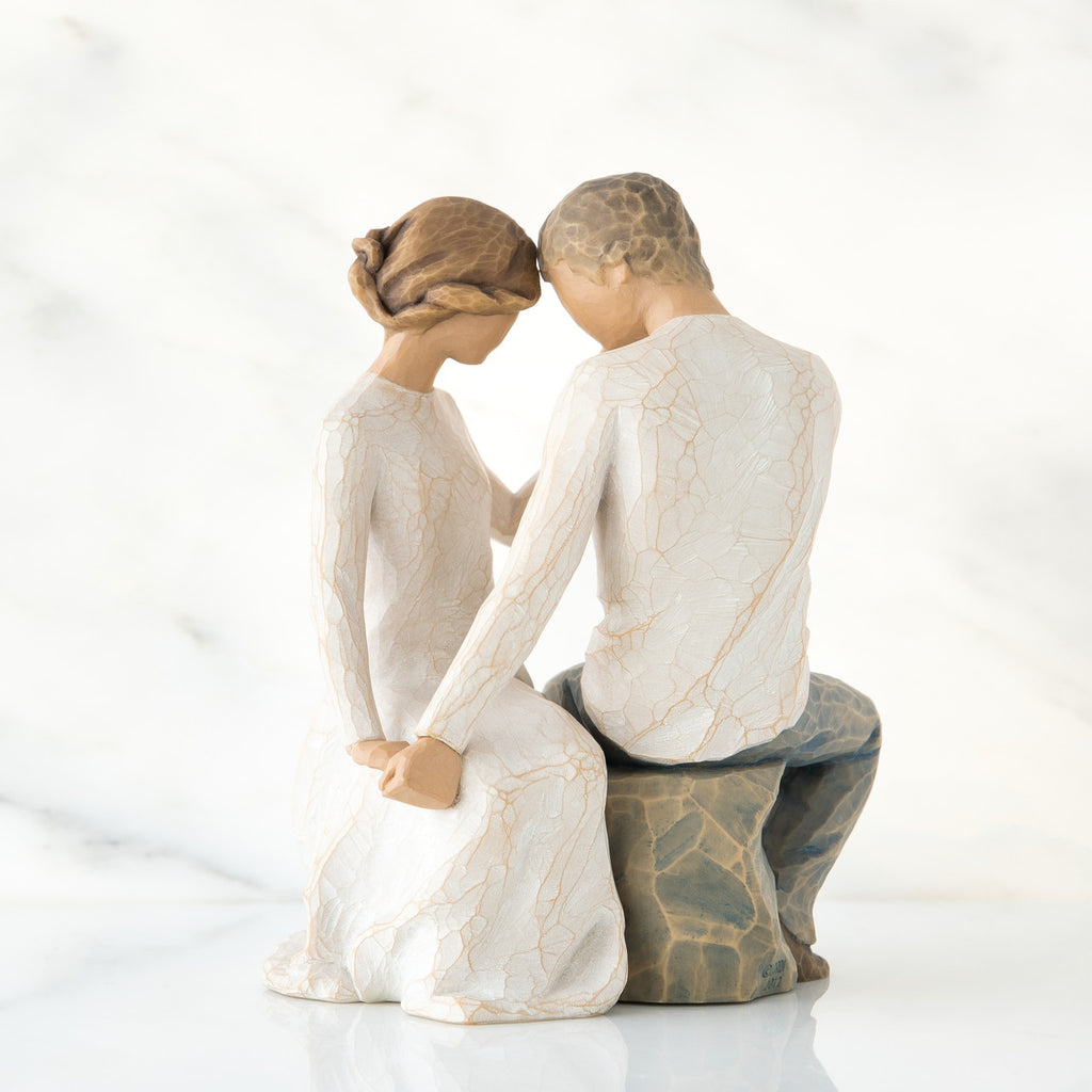 Man and woman figurine in white sitting on rock holding hands facing one another