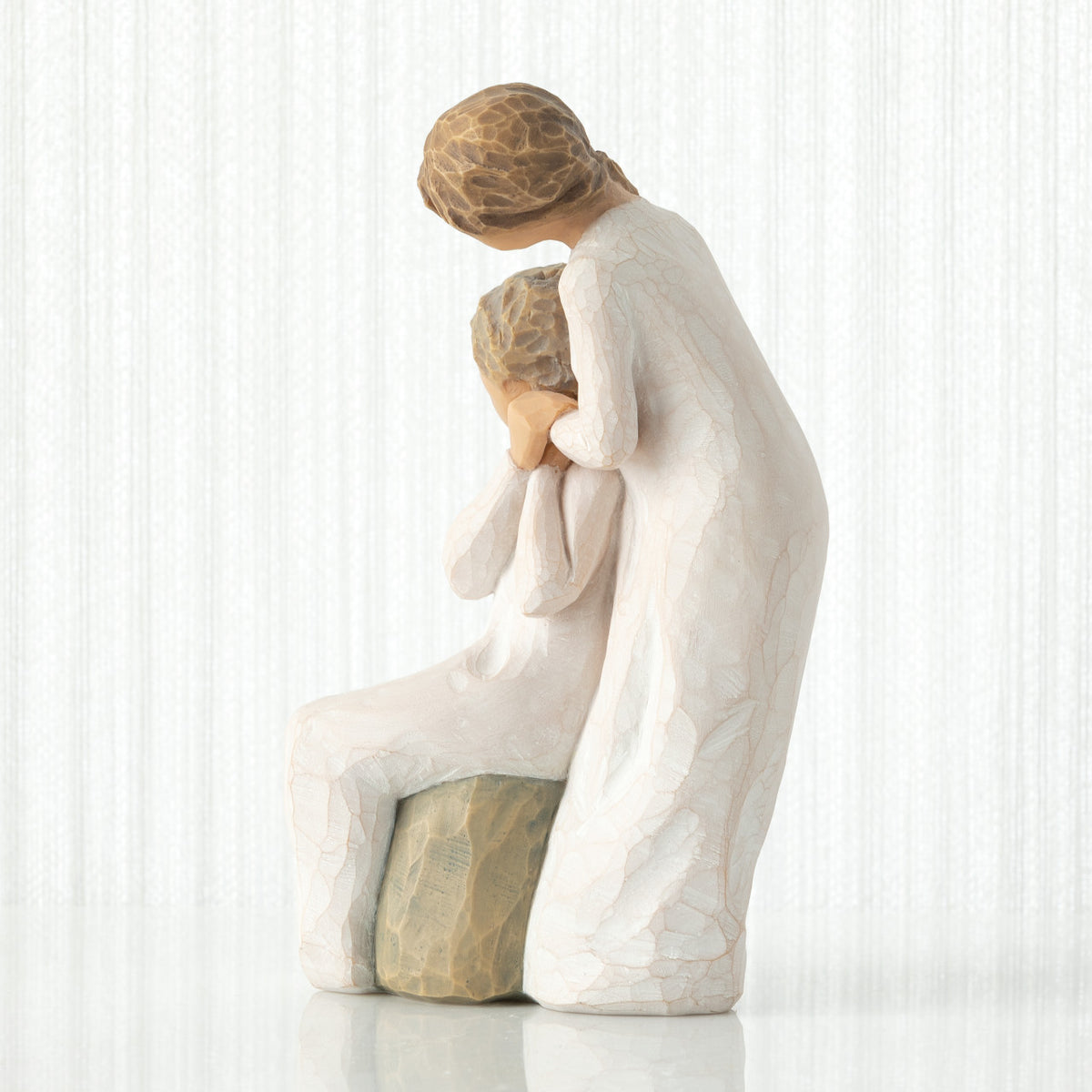 Left-facing view, seated older female in cream dress, with younger female in cream dress, standing at her shoulder, hands embracing
