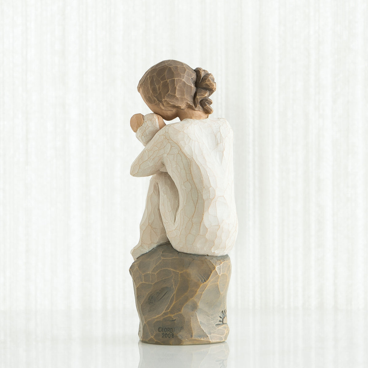 Back view of brunette girl sitting down on a rock wearing white shirt holding a baby