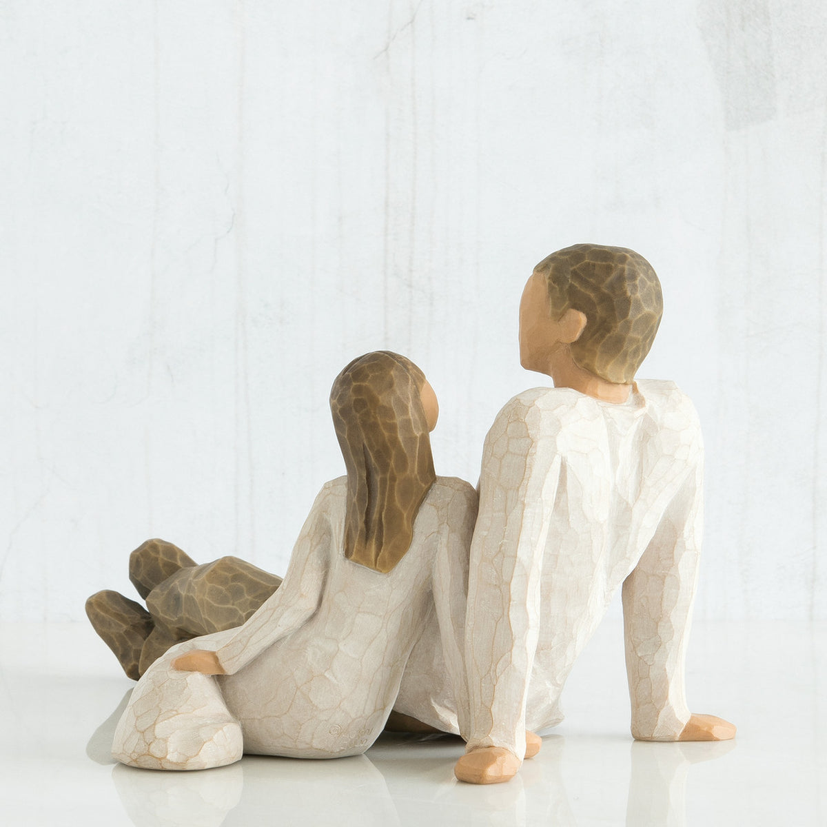 Back view of father figurine sitting next to daughter figurine - both wearing white