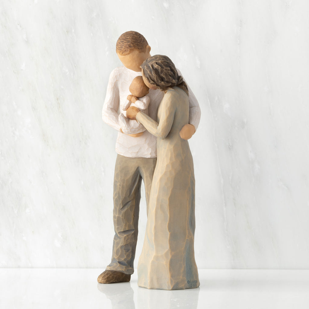 Left view of standing couple, woman has darker skin and hair; man has lighter skin and hair, holding a baby between them.