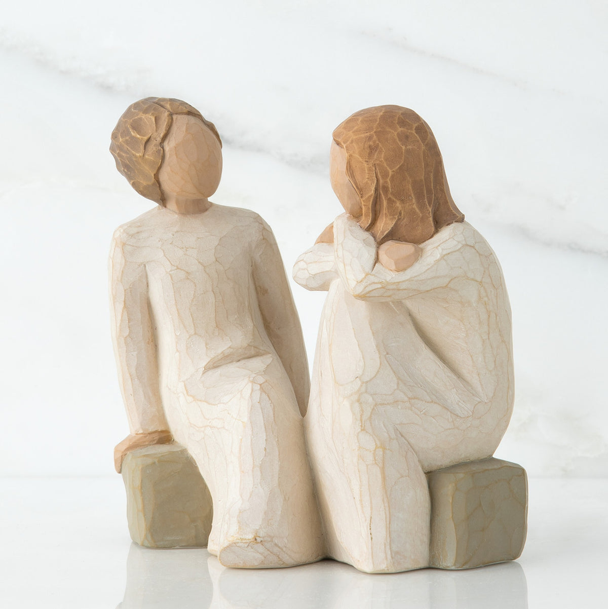 Two red haired girl figurines in white dresses sitting down on rocks