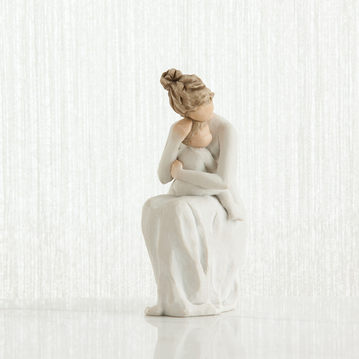 Brunette woman figurine in white dress sitting hugging baby figurine - all white background