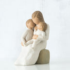 Mother figurine in white dress sitting on rock holing her two baby figurines in her lap