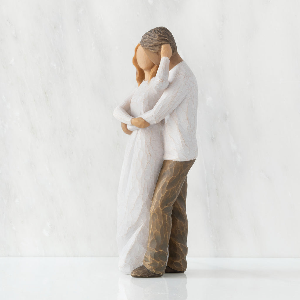 Left view of couple, standing with arms around each other. Woman has lighter skin and hair; man has darker skin and hair.