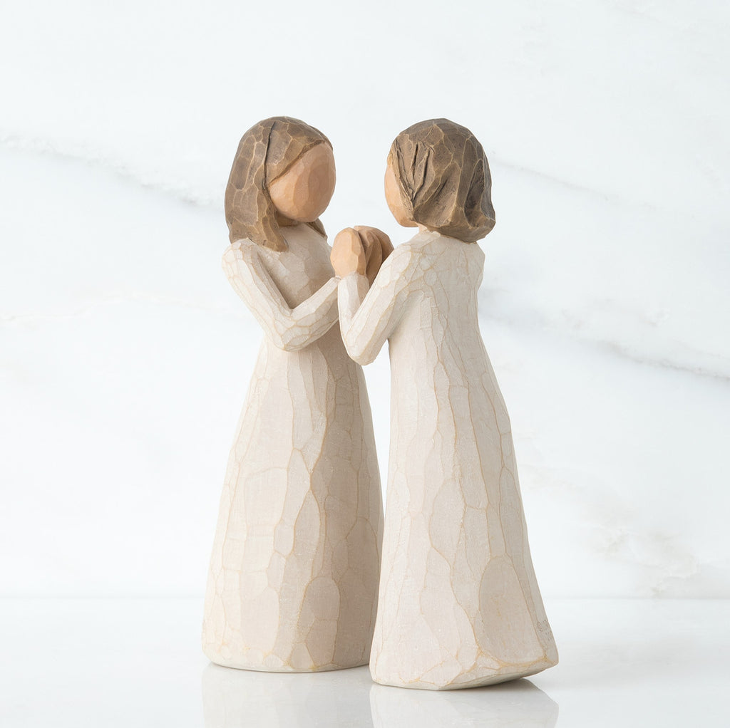 Two young girl figurines in white holding hands facing another