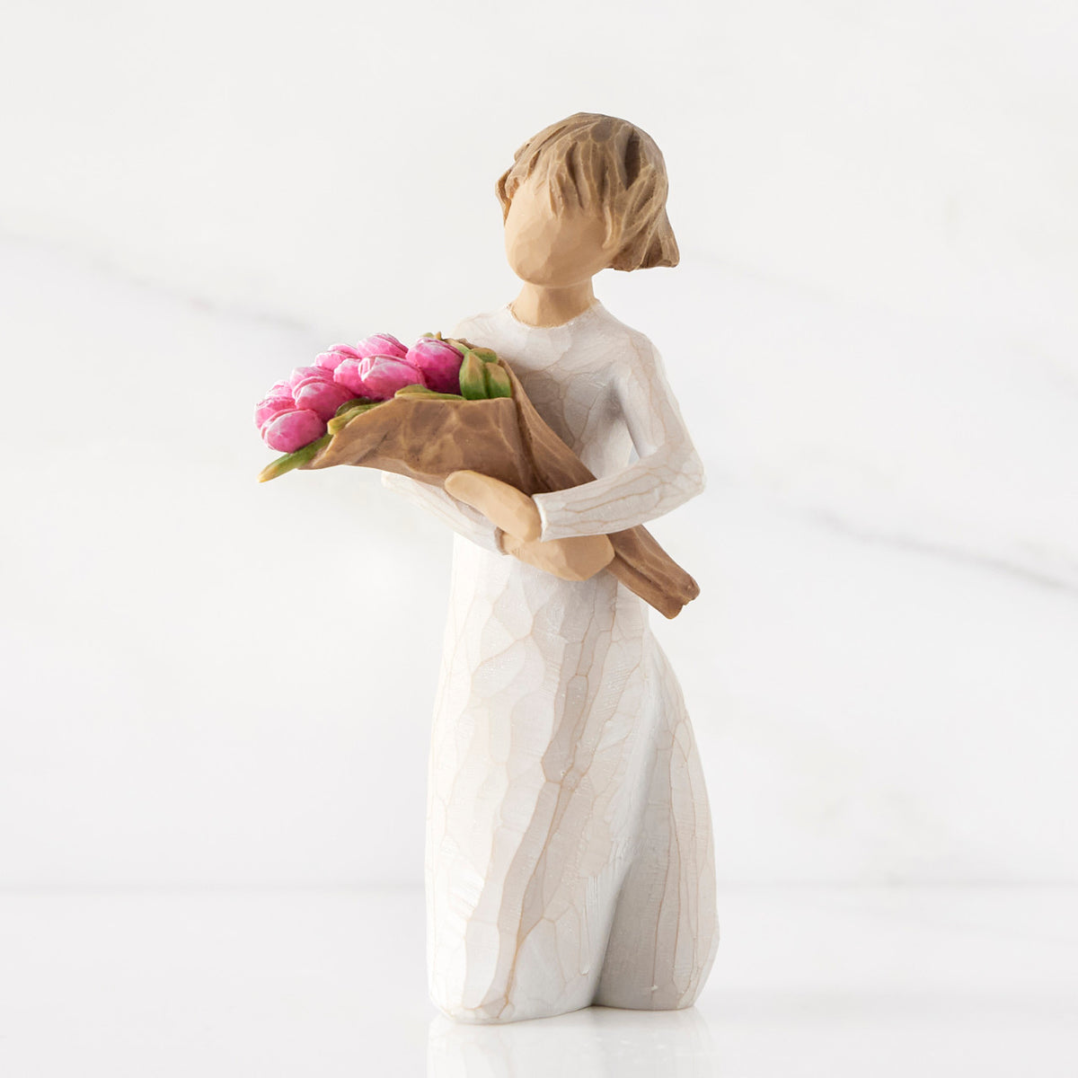 Left side of standing figure in cream dress holding bouquet of pink tulips