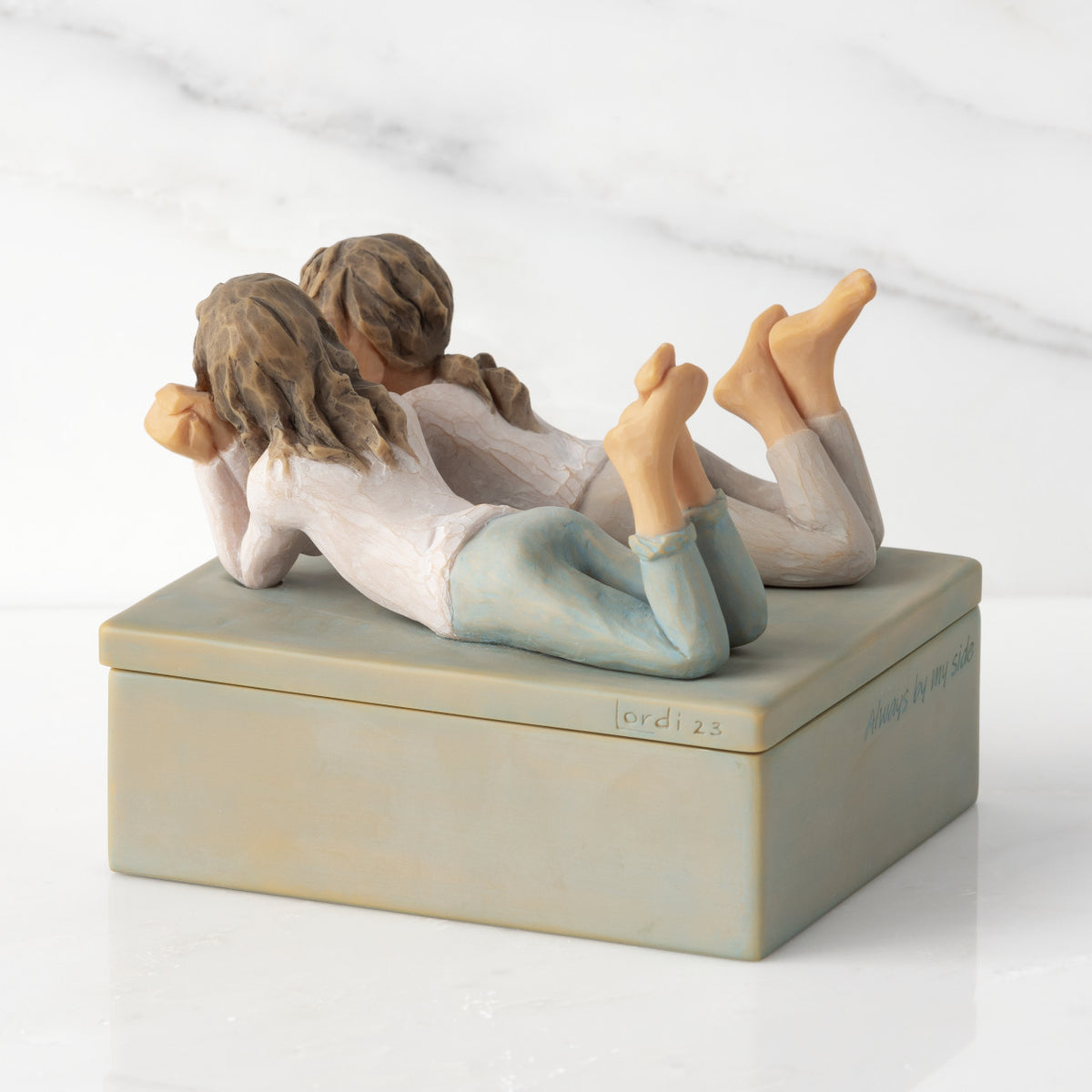 Back/left view of closed rectangular blue-gray resin box, sculpture of two girls affixed to lid
