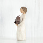 Side view of brunette figurine in white dress holding brown house figurine