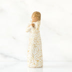 Gold haired woman in white/gold dress facing forward with arms to her chest