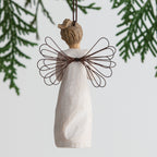 Back view of angel ornament with brown hair in high pony tail leaning forward and holding a red apple up to her face with both hands. Brown string attached to top of angel ornament