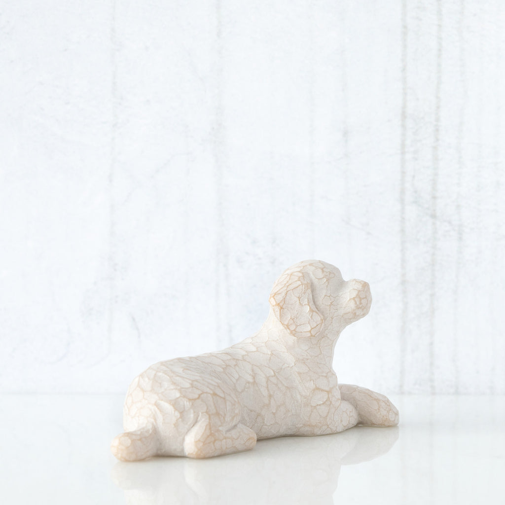 Figure of small white dog laying down with paws crossed in front, facing right