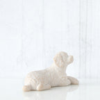 Figure of small white dog laying down with paws crossed in front, facing right