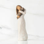 Left view, standing female figure in cream dress, holding dark color puppy in her arms