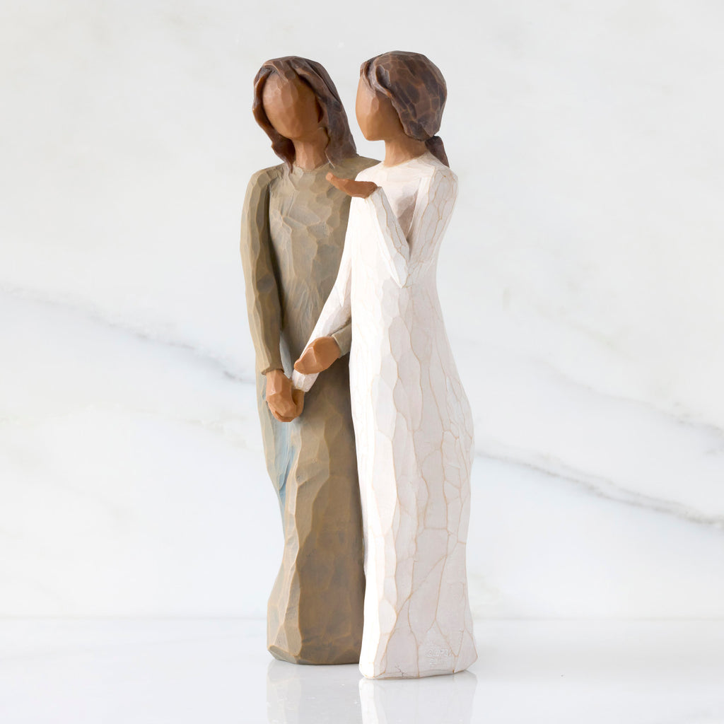 Left-facing view: Figure of two women with darker skin tones in different colored dresses, standing arm in arm