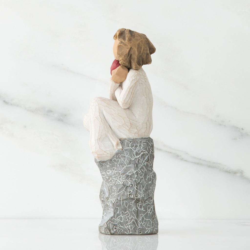 Side view of young girl in white sitting on grey rock with her hands up to her face