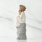 Side view of young girl in white sitting on grey rock with her hands up to her face