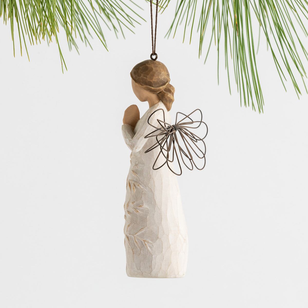 Side view female figure with wire wings in cream dress carved with a tree design, holding hands in prayer, ornament loop attached to head