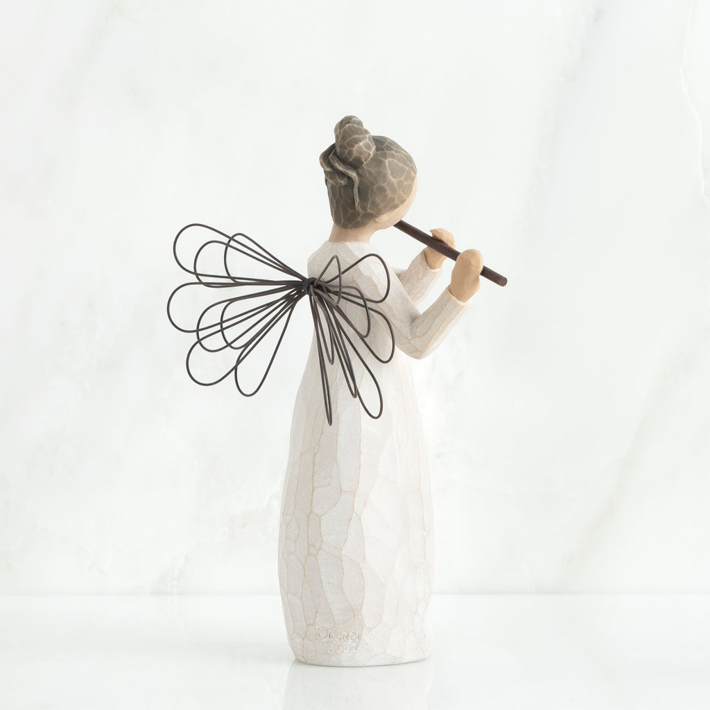 Back view of brunette angel figurine in white dress, black wings, and playing the flute
