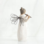 Back view of brunette angel figurine in white dress, black wings, and playing the flute