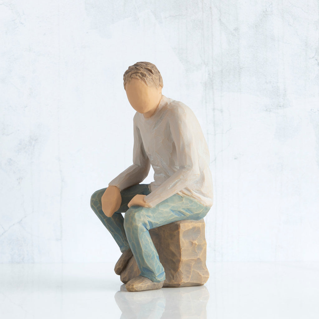 Left-facing view, adult male figure in light gray shirt and blue jeans, seated on gray rock