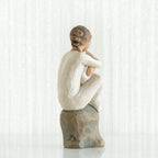 Back view of brunette girl figurine sitting down in white dress on rock