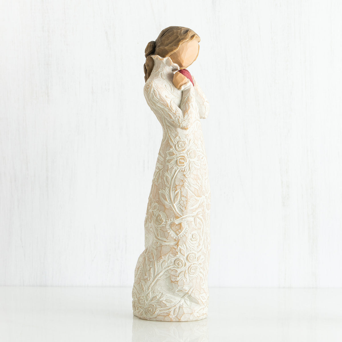 Side view of brunette girl figurine in white dress holding pink hear figurine