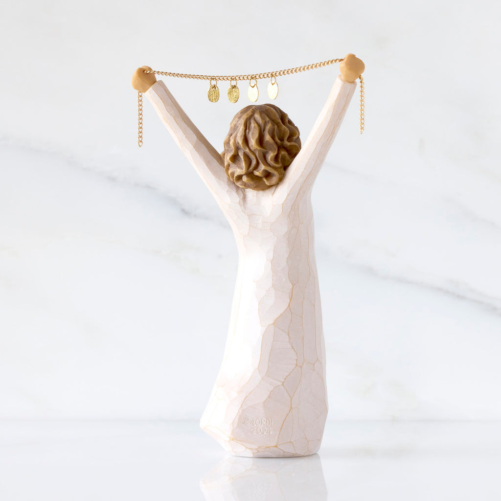 Willow Tree Courage 2025, back view of 6”h hand-painted standing figure in cream dress holding aloft a gold chain with 2025 etched on gold medallions