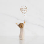Back view: standing figure in cream dress, arms raised, holding gold wire balloon with 2024 written in gold wire inside