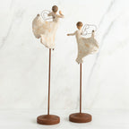 Two angel figurines in white dresses on wooden stands