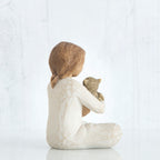 Back view of young girl with light brown hair sitting cross legged and holding a brown cat in her arms, both cat and girl gaze at each other