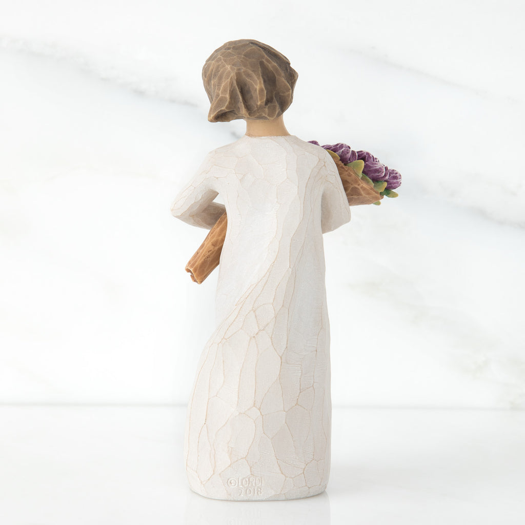 Standing figure with short brown hair wearing long cream dress holding large bouquet of purple tulips, facing back